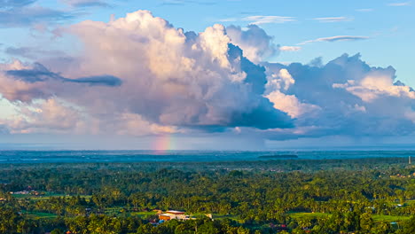 cloud formation timelapse with rainbow in sky over bali rural tropical landscape at sunrise, green fields, aerial view