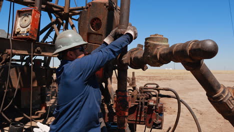 man in uniform, helmet, sunglasses and protective gloves hits a nut on the pipe with a sledgehammer. worker unscrews the spacer with his hands.