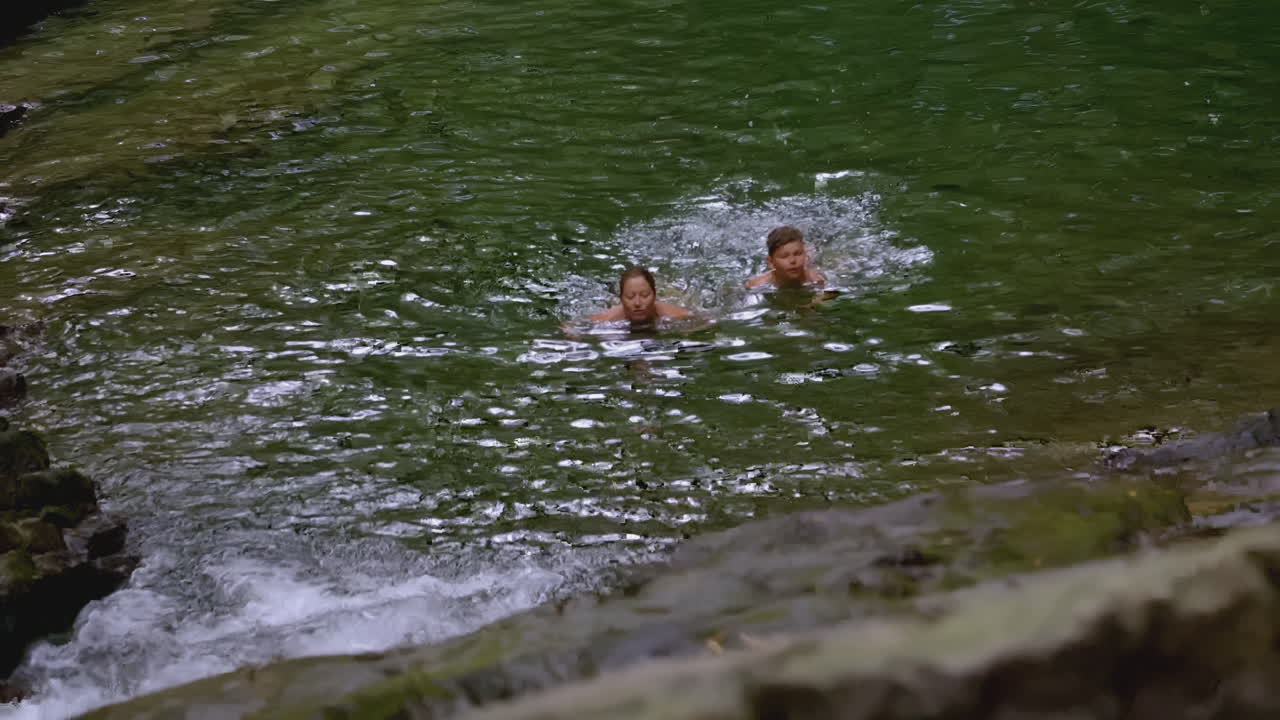 dos personas nadando en una piscina natural con cascadas
