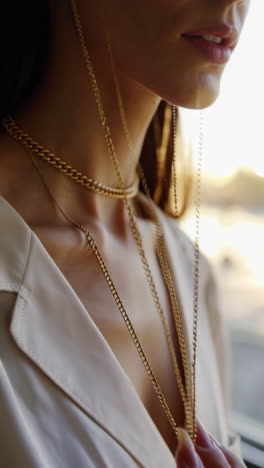 close-up of a person's hand and neck adorned with elegant gold chains and rings in warm light