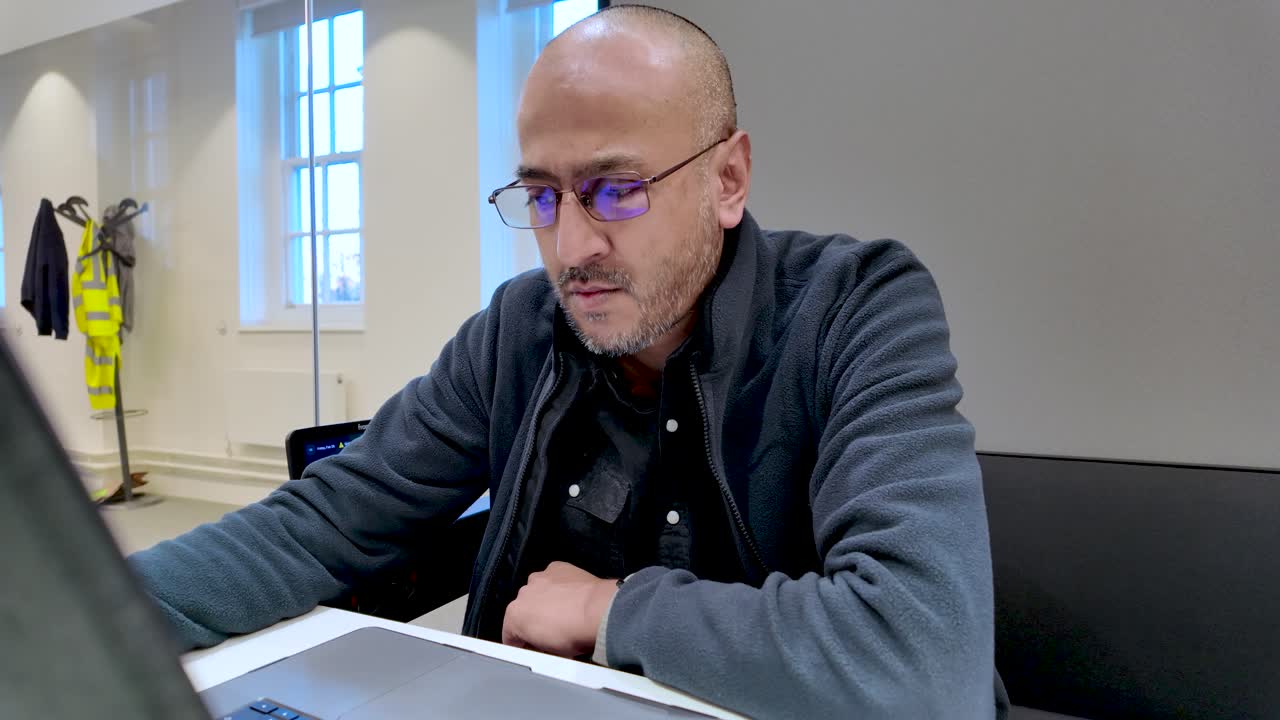 South Asian male professional concentrating on his laptop in a bright, contemporary office space, demonstrating workplace productivity