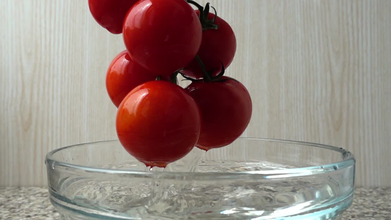 Der Koch nimmt Tomaten aus einer Schüssel mit Wasser. Zeitlupe.