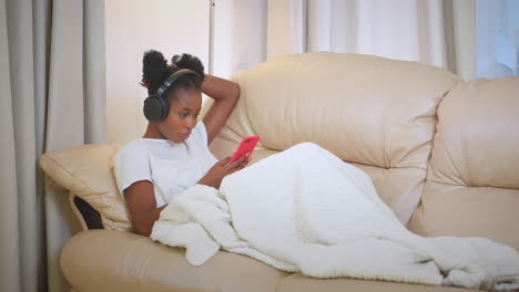 woman relaxing on a couch with headphones and phone