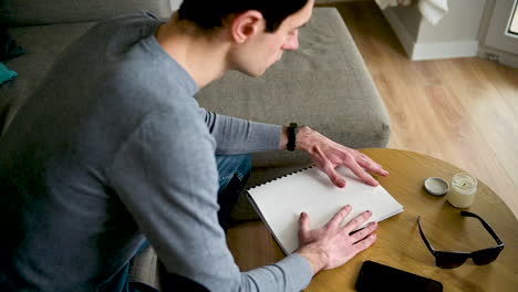 ciego leyendo un libro en braille mientras se sienta en el sofá en casa 3