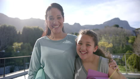 Happy-biracial-mother-and-daughter-with-yoga-mats-embracing-on-terrace-in-sunny-day,-slow-motion