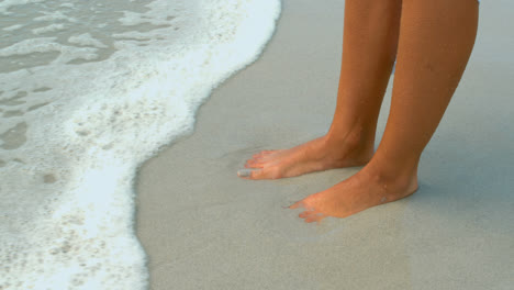 Low-section-of-woman-foot-touched-by-gentle-sea-surf-on-the-beach-4k