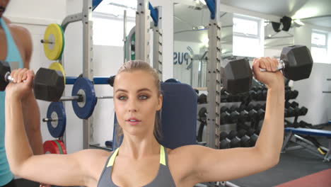 mujer joven levantando pesas con un entrenador en un gimnasio
