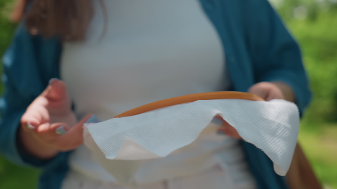 Joyful woman in casual outfit dancing outdoors holding embroidered fabric she created, sunlight illuminating delicate threads, green park background radiating warmth