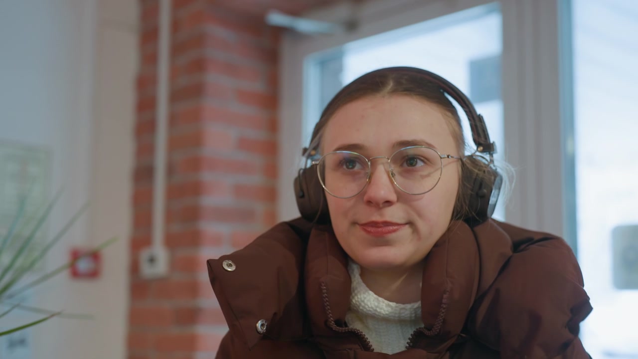 Thoughtful Young Woman in Headphones and Glasses Indoors