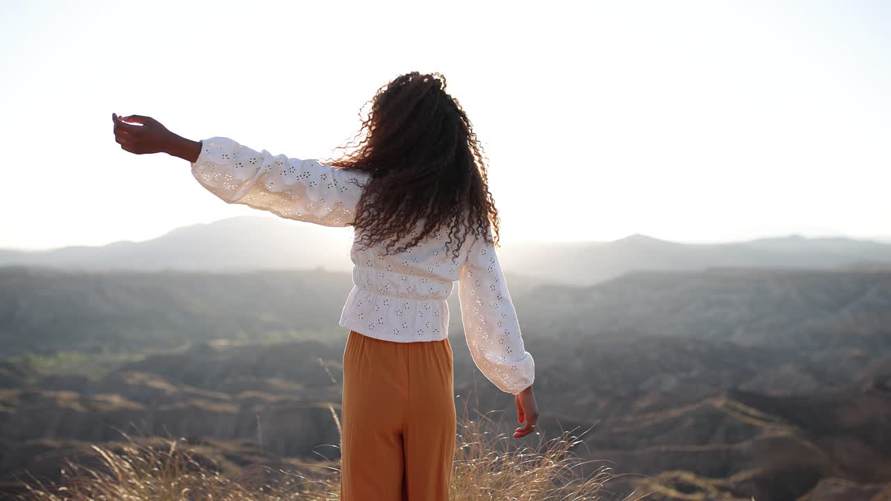 Woman with Curly Hair Enjoying the Sunset in a Vast Desert Landscape