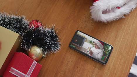 niño caucásico con sombrero de papá noel y jugando con el globo de nieve en la videollamada de navidad en el teléfono inteligente