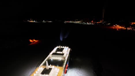finnlines hybrid roro ship finnsirius moving through ice covered sea at night. harbour lights ahead. searchlight illuminated. aerial view moving over the vessel.