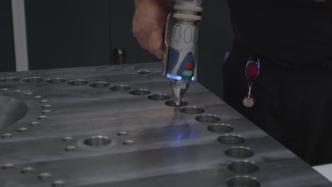 beautiful close up of a man in a factory using a handheld honing tool to hone out holes in a large metal block