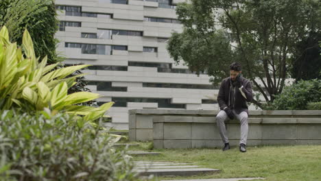 Trendy-well-dressed-male-sit-on-a-bench-in-residential-district-area-having-a-phone-business-call-with-his-modern-smartphone