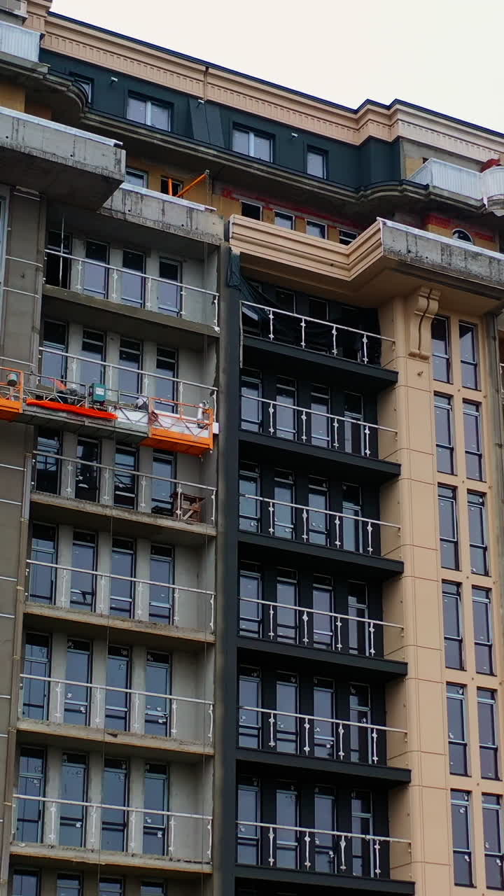 Building of new tower architecture. Modern multi storey building under construction. Front view of a high-rise building. Workers build the tall house. Vertical video