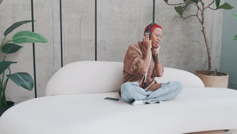 joven afroamericana escucha música en auriculares y canta sentada en el sofá
