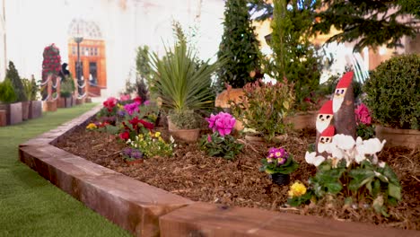 hermoso jardin, lleno de hermosas y coloridas flores, cesped verde, todo hermoso, unos papa noel tallados en madera, trabajo perfecto