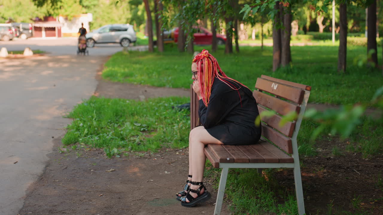 Mujer sentada en un banco observando pensativamente una escena callejera; mujer informal con trenzas rosas mirando el tráfico que pasa; retrato de una mujer con trenzas rosas vibrantes contemplando la vida urbana al aire libre