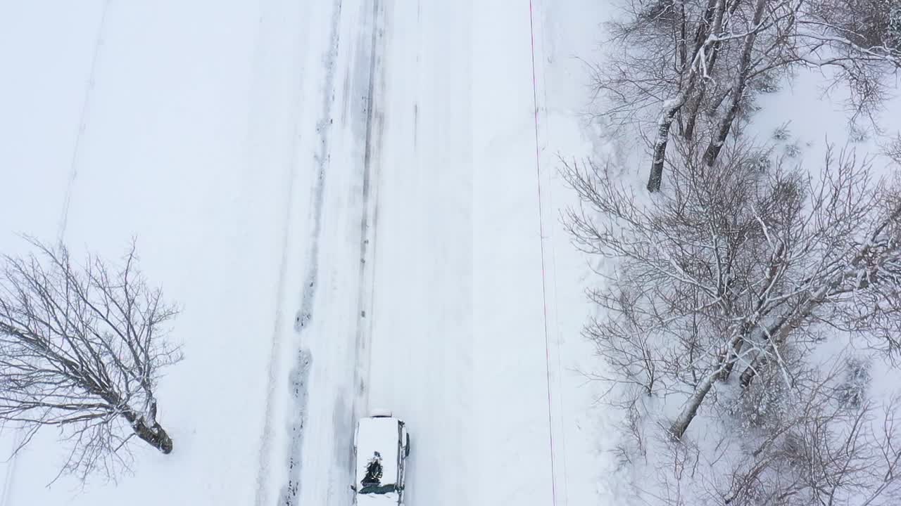 블리자드 하향식 슬로우 모션 공중에서 도로를 따라 운전하는 눈 덮힌 suv 위로 뒤로 비행