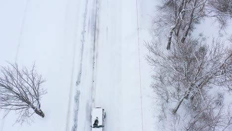 flying backward above a snow covered suv driving down a road during a blizzard top down slow motion aerial