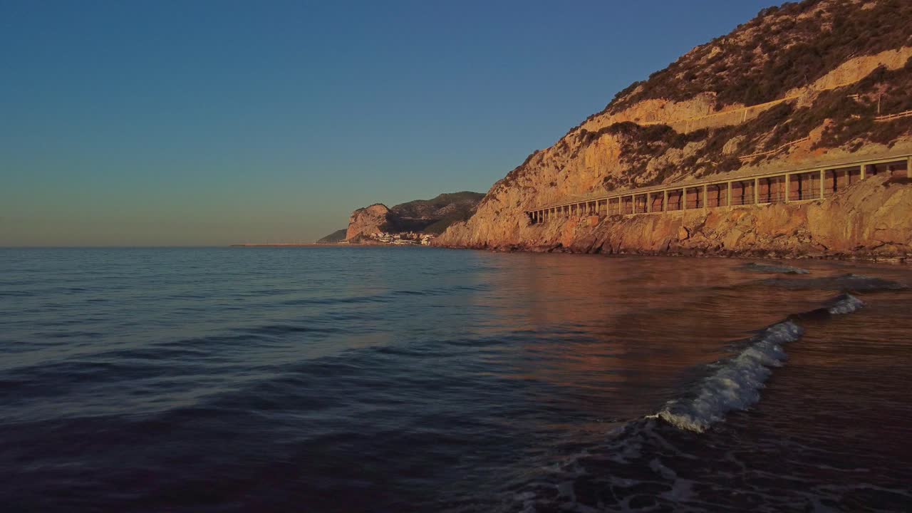 Golden sunrise at Port Ginesta beach, Barcelona, with tranquil waves and rocky cliffs