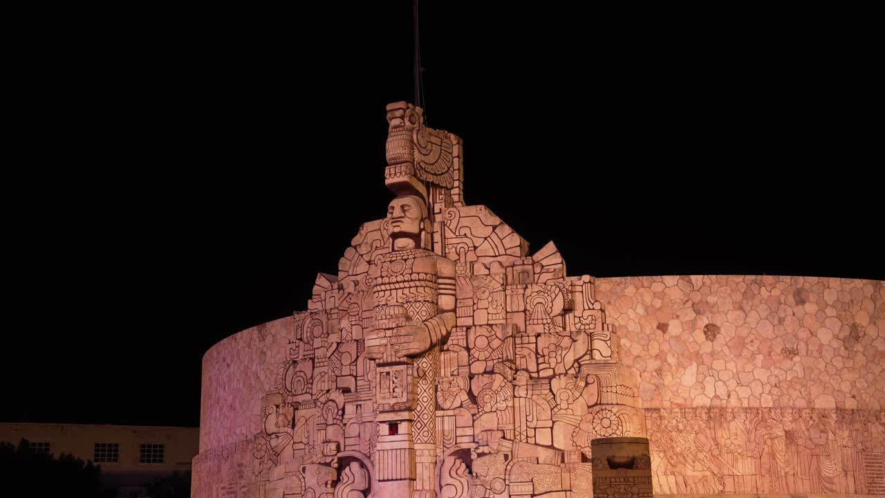 Nighttime view of the Monument to the Fatherland in Merida, Yucatan, showcasing its intricate Mayan-inspired carvings and grand illuminated stone facade