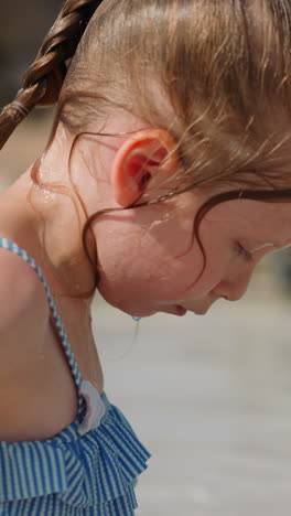 thoughtful little girl in swimsuit with ruffles rests on beach at exotic marine resort on sunny summer day close side view slow motion