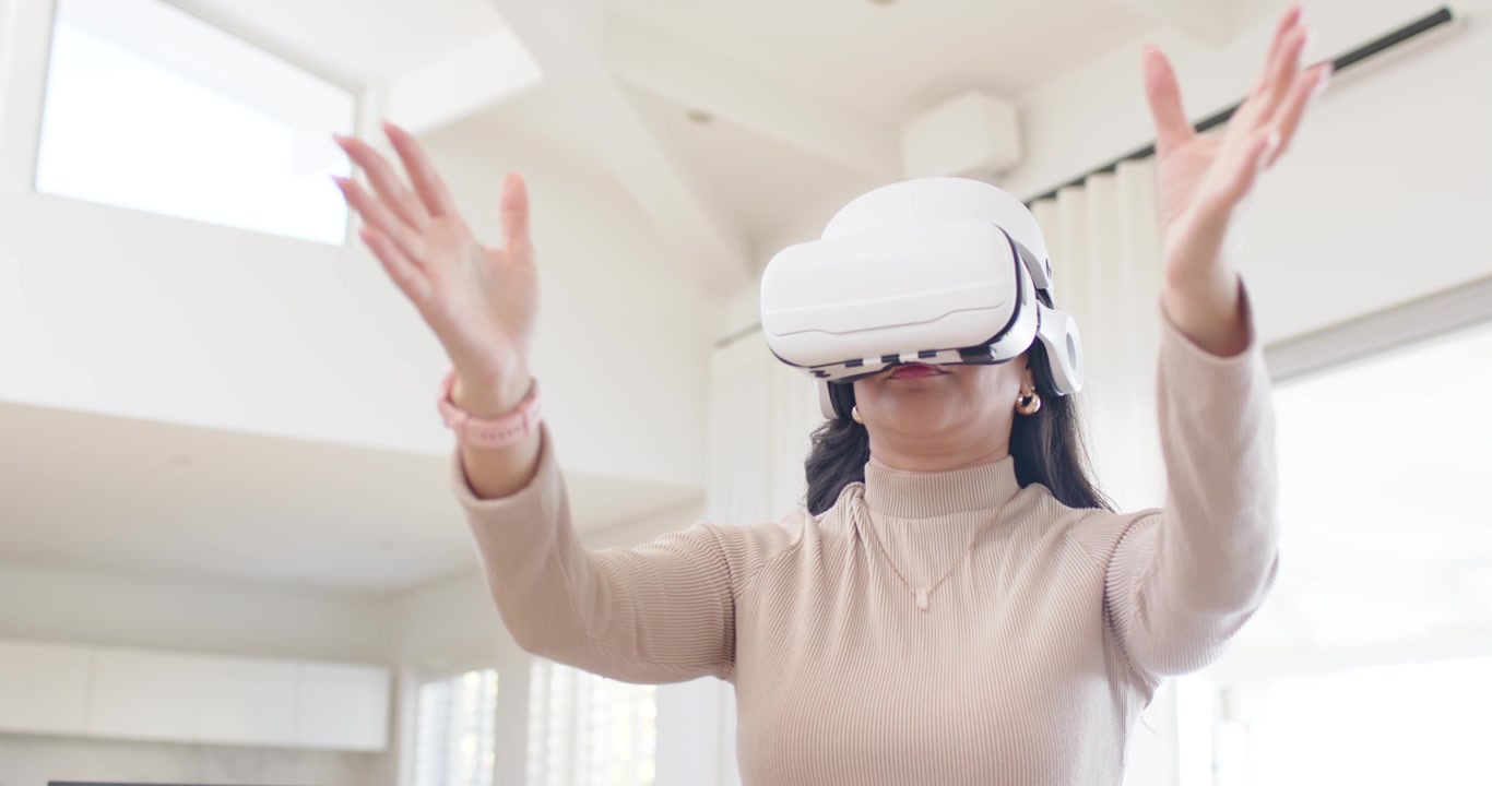 Amiche diverse, donna con visore VR che gesticola in casa mentre un'amica offre dispositivi per unirsi