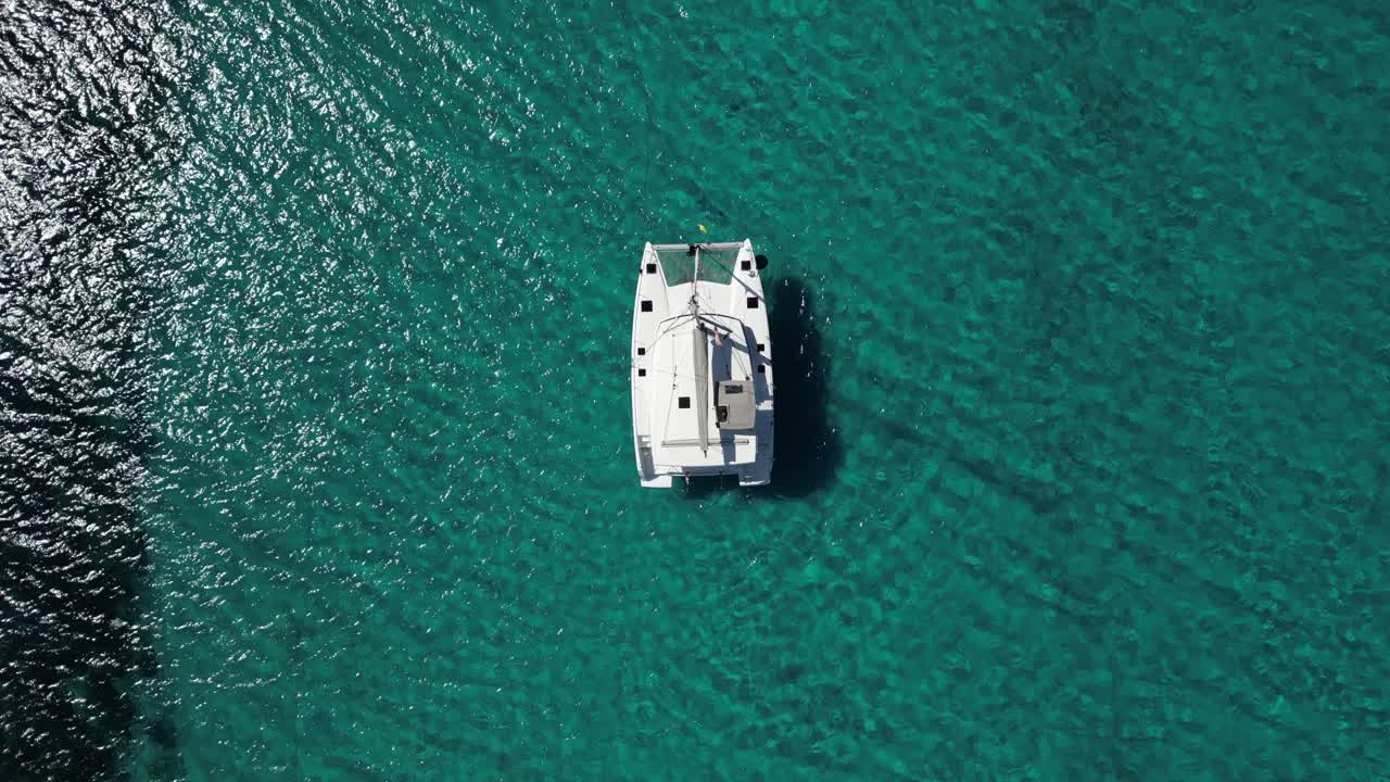 barco de catamarán con brillo de sol en el agua turquesa clara, aérea