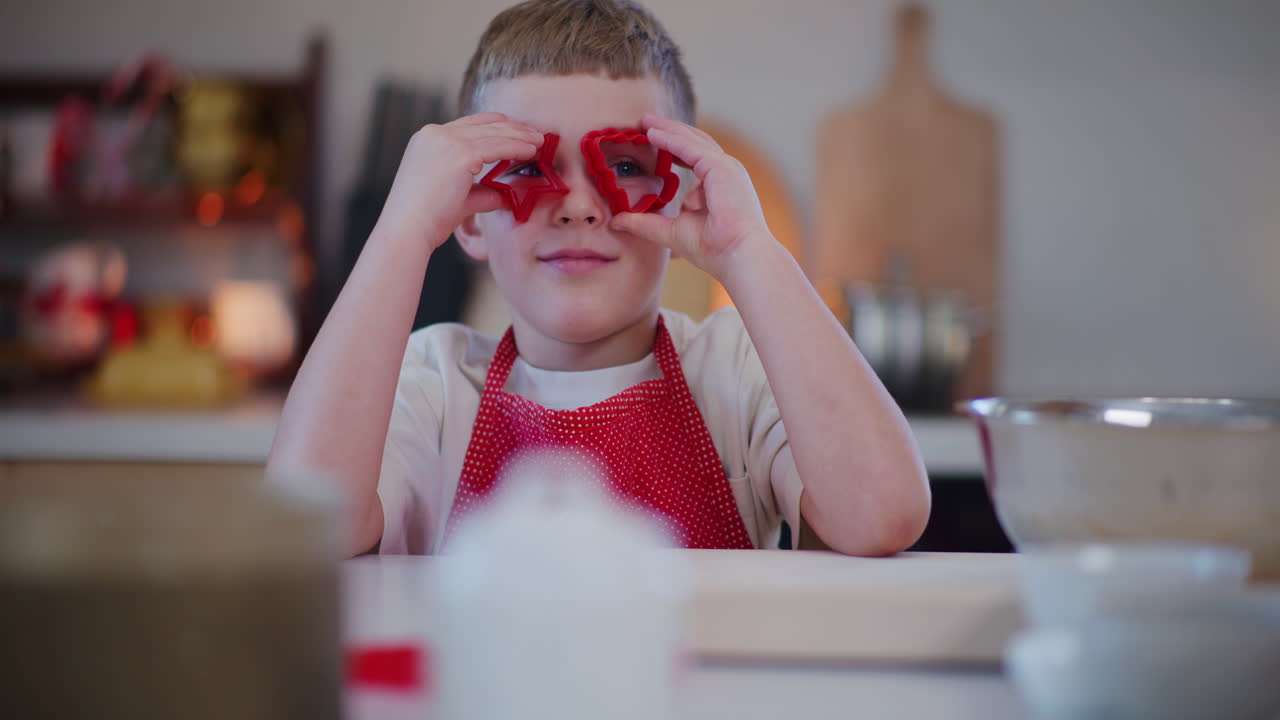 niño mira a través de cortadores de galletas y disfruta de hornear