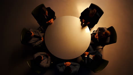 overhead view of a business meeting around a round table with dramatic lighting
