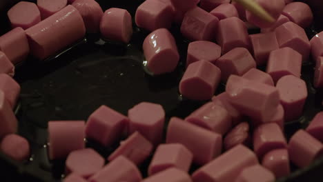 macro close up view: pink wiener pieces are fried in hot buttered pan