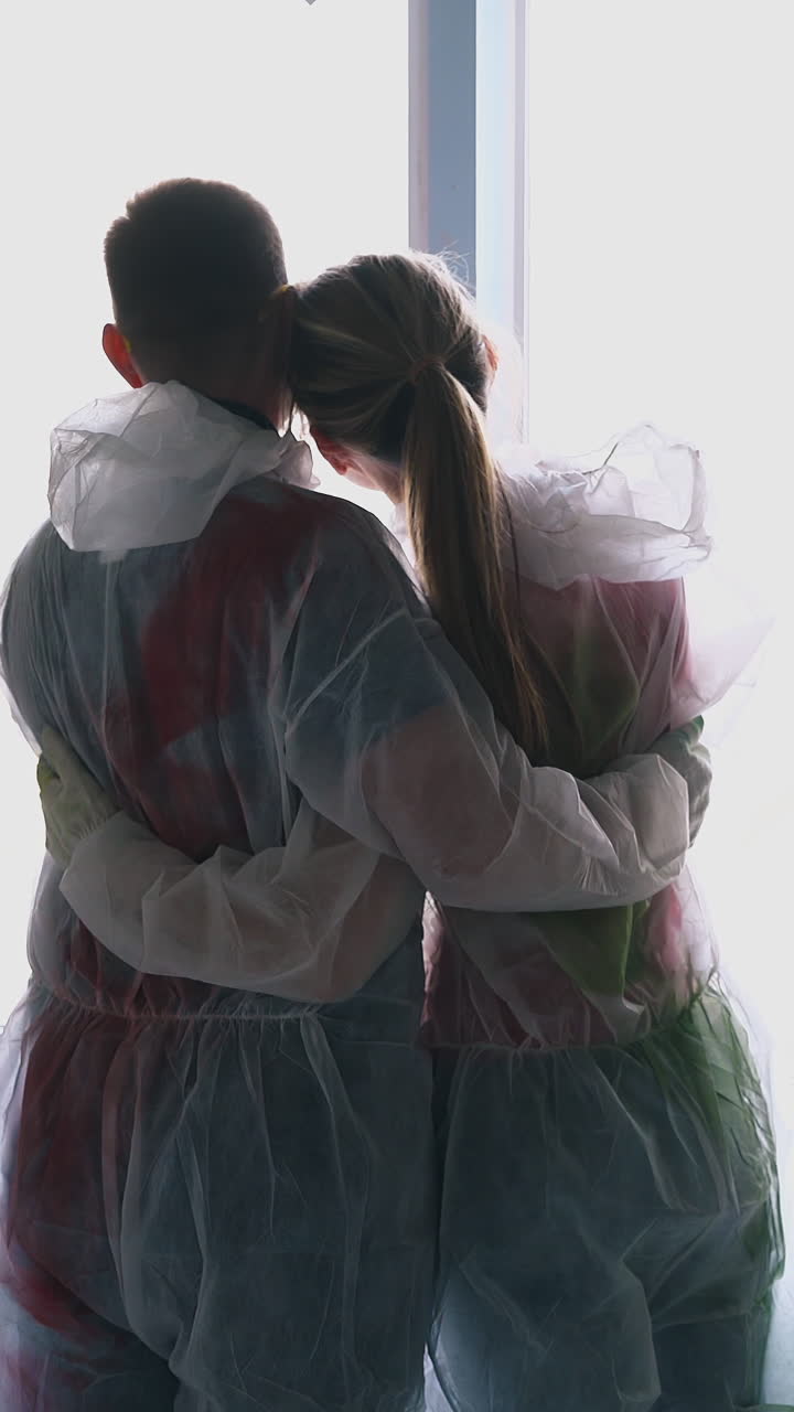 positive young family of happy girl and bearded guy in transparent coveralls dances hugging near window in spacious room