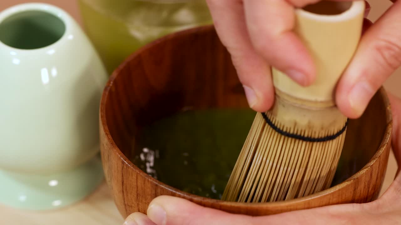 Hand whisking matcha green tea in wooden bowl, minimal style, soft natural lighting, close-up