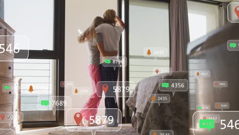 animation of social media icons on banners over caucasian couple in love embracing in hotel room