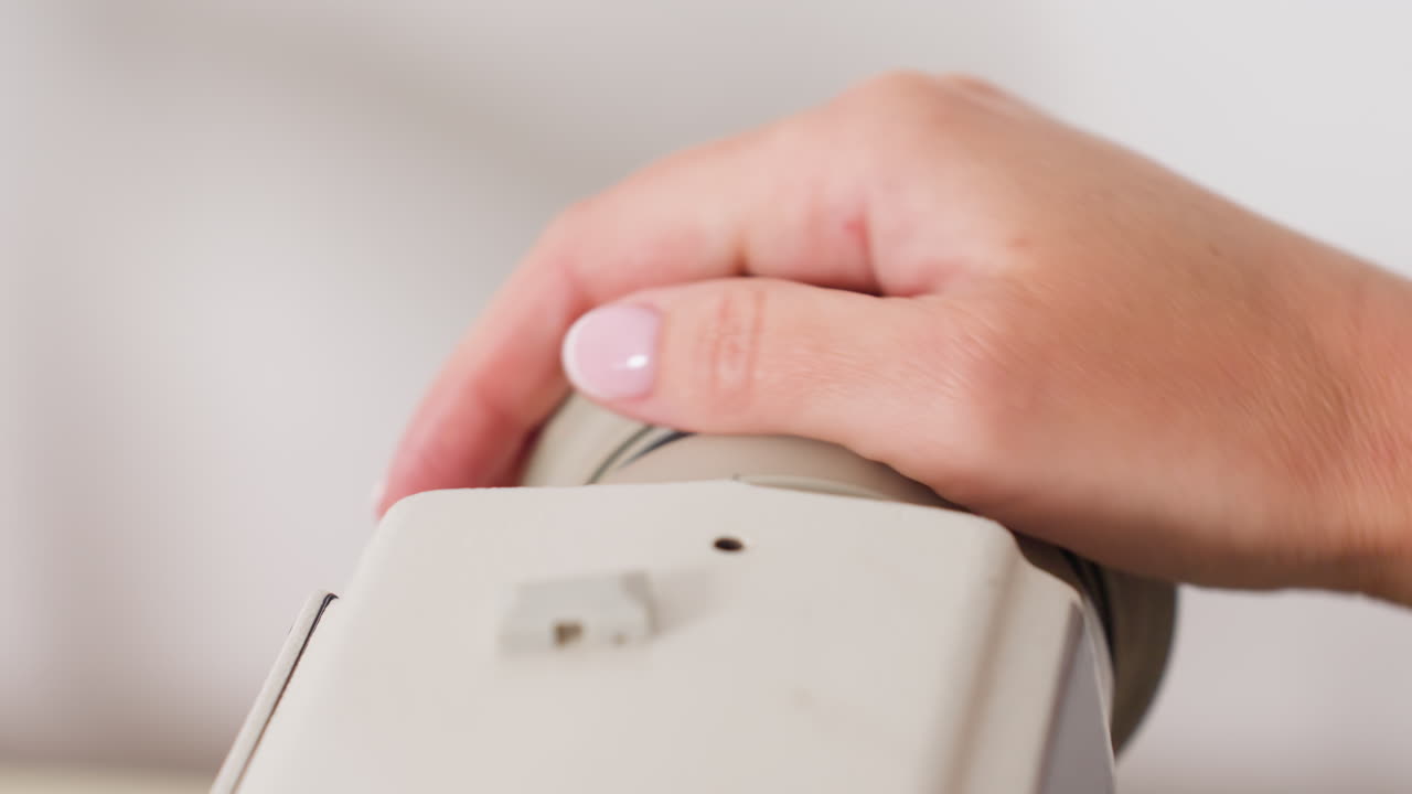 Garment maker places hand on balance wheel of electric machine, adjusting motion, controlling pace, ensuring smooth operation, focusing on precision, maintaining professional technique