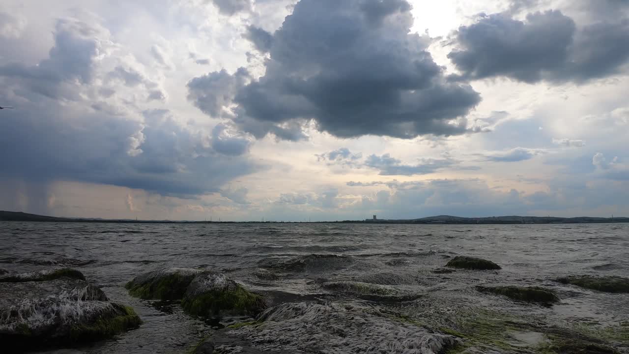 Beautiful view from stones in the water around the calm sea. Stormy fast moving clouds of approaching storm. Green algae in the sea water. Afternoon near Kraimorie. Black Sea, Bulgaria.