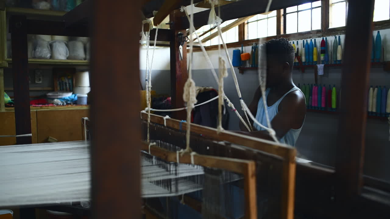 a young man operating a floor treadle loom inside