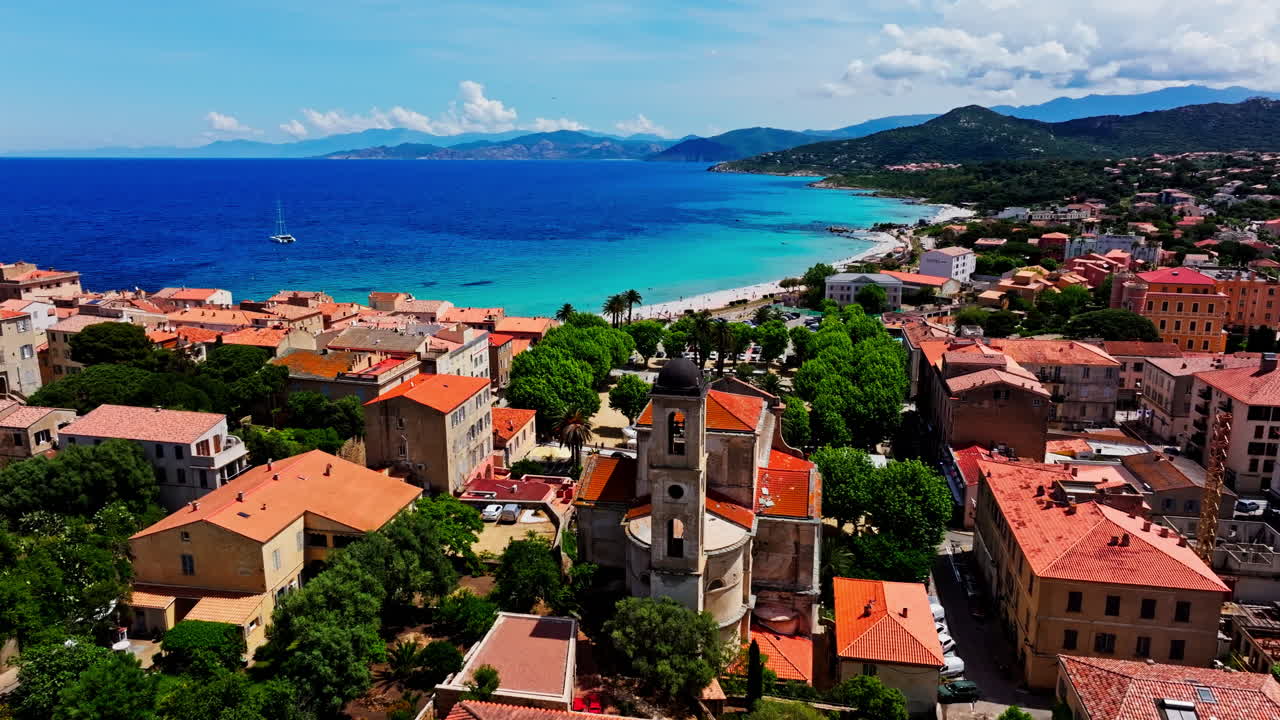Aerial drone shot over the coastal town Île-Rousse in the Balagne region in Corsica, France. View of the beach and turquoise sea in the distance. Summer holidays destination