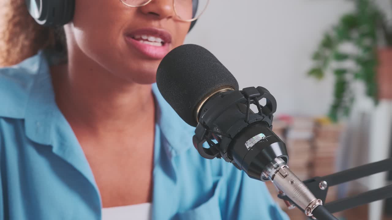 Giovane donna afroamericana legge un testo al microfono seduta in uno studio di registrazione.