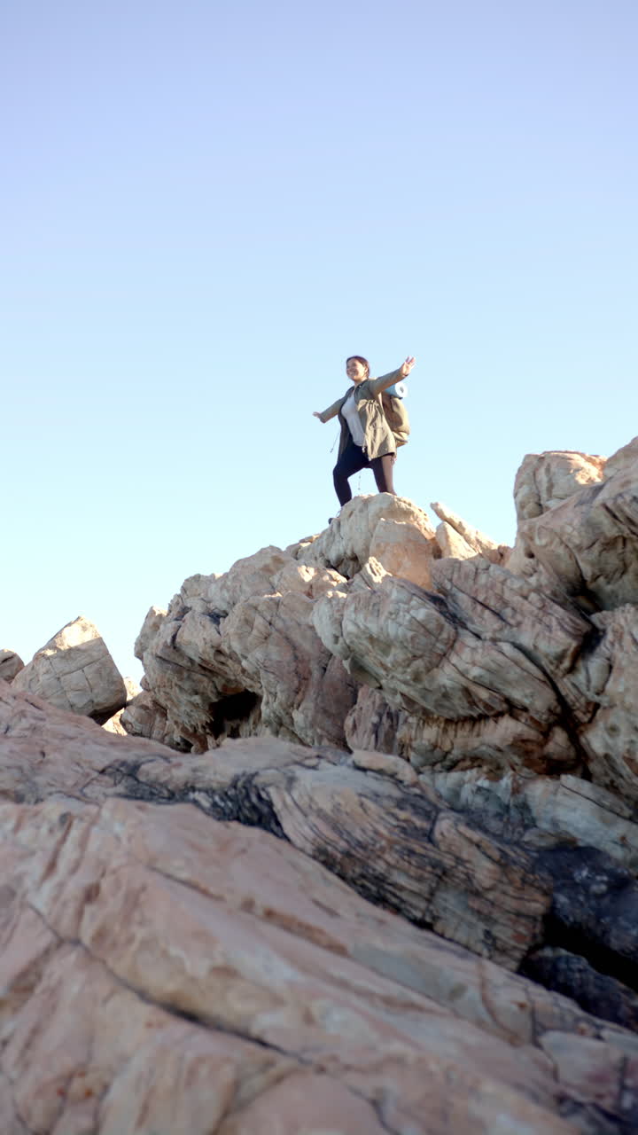 Vertical video: Hiking on rocky mountain, woman with backpack raising arms in triumph