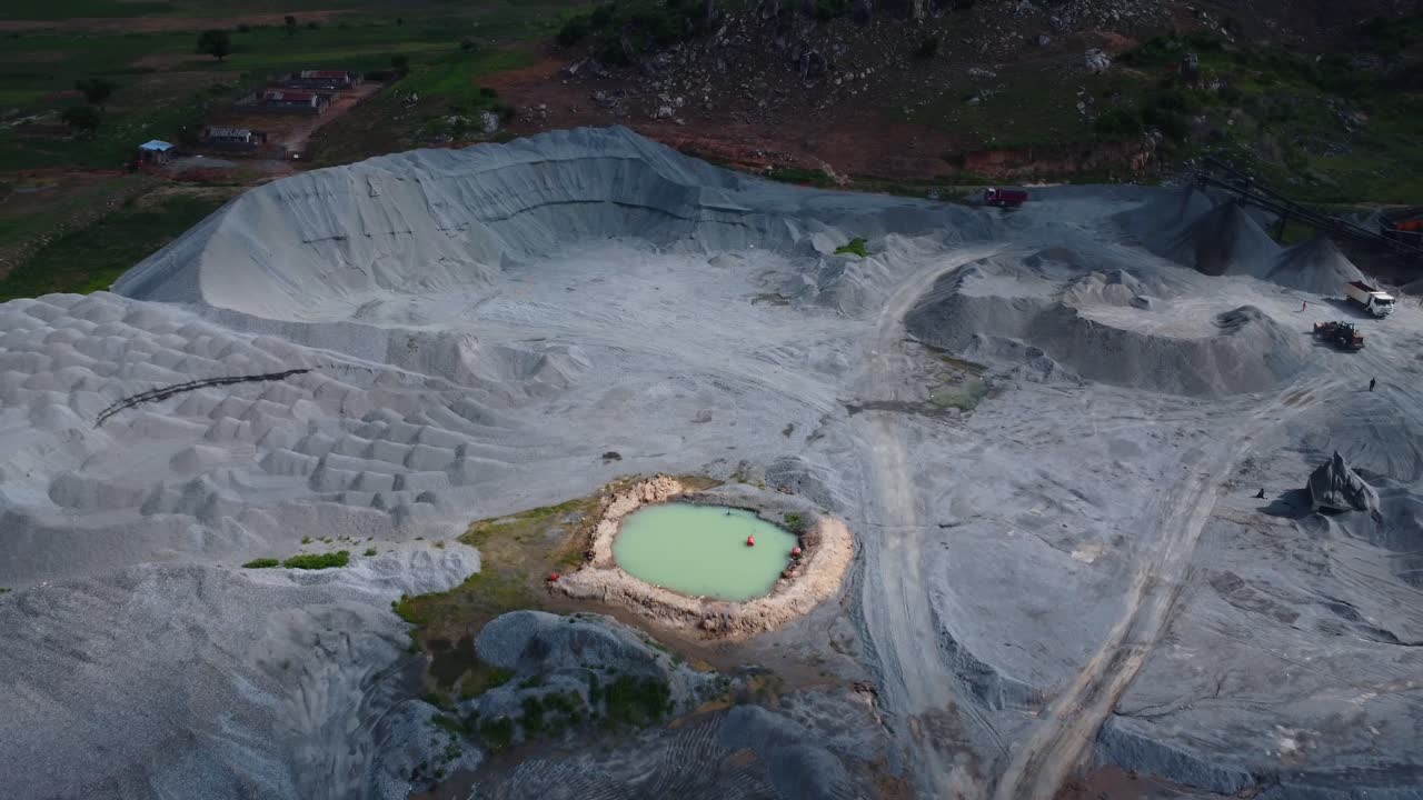 An expansive aerial view of a quarry with a striking turquoise pond at dusk. The rugged terrain under soft evening light creates a mysterious, tranquil atmosphere in this unique landscape, Africa