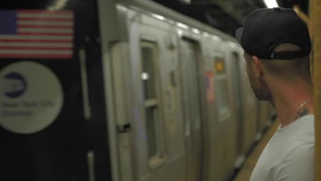 caucasian man with black cap looking at subway arriving at subway platform in new york city.