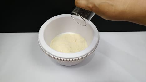 a woman is adding ice cream powder to milk into the pan to start mixing them and make ice cream