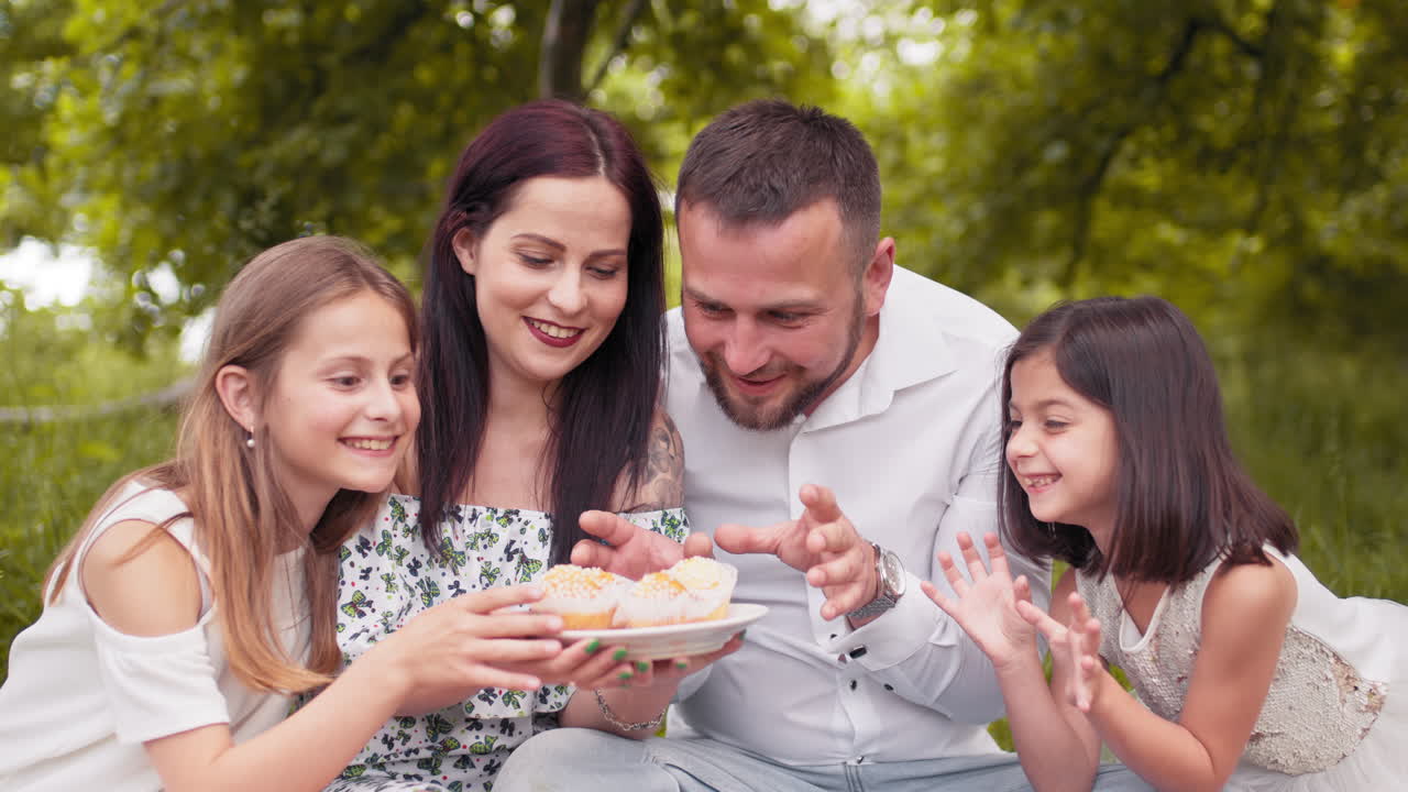 행복 한 가족 이 공원 에서 피크닉 을 하면서 컵케이크 를 즐기고 있다