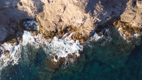 Vista-Aérea-De-Fondo-Lateral-De-Las-Olas-Rompiendo-Contra-Las-Rocas,-Agua-Turquesa,-Cerdeña,-Italia,-Destino-De-Viaje-De-Vacaciones-De-Verano