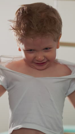 little boy tears t-shirt showing courageous and power against punching bag and ladder slow motion. toddler fighter damages clothes as challenge in gym