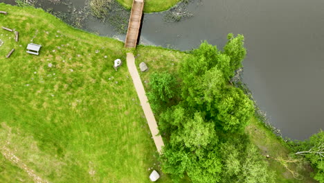 a top-down aerial view of a bridge crossing a small waterway surrounded by grassy areas and trees