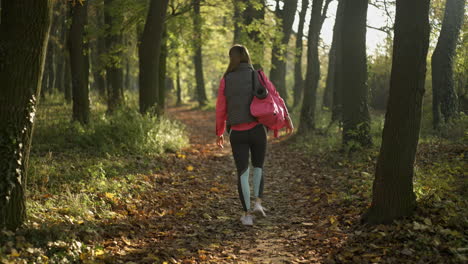 woman walks on a path in an autumn forest carrying a yoga mat