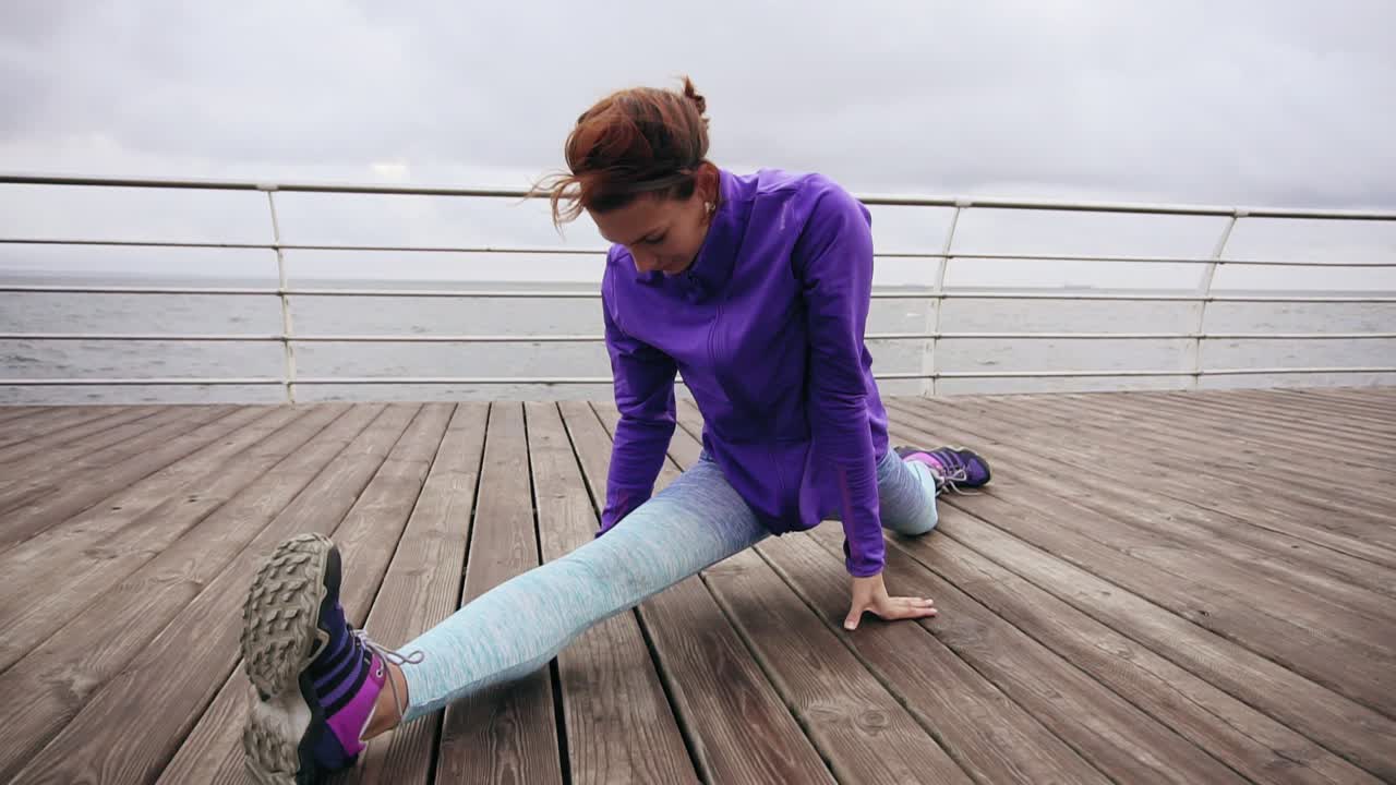 Close up view: Athletic woman stretching her legs before a jog on the beach by the sea early in the morning. Young girl doing